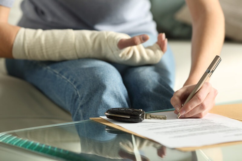 woman with bandaged arm signing paperwork