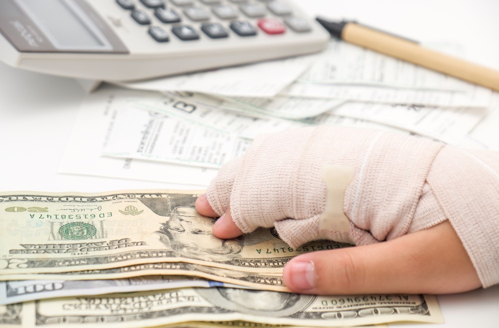 A person’s hand wrapped in a bandage next to a stack of cash and a calculator.
