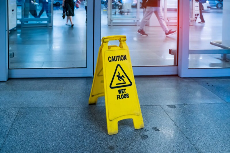 People walking behind a yellow wet floor sign.