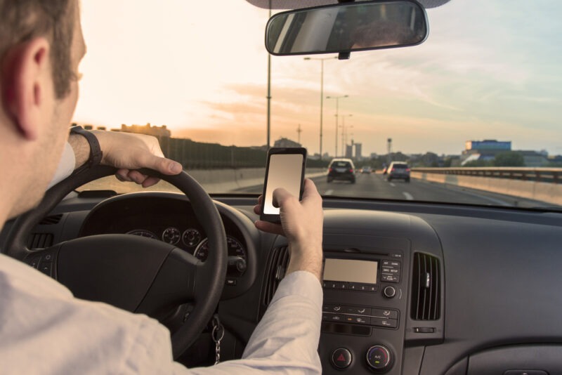 a man looking at a cell phone while driving on the freeway