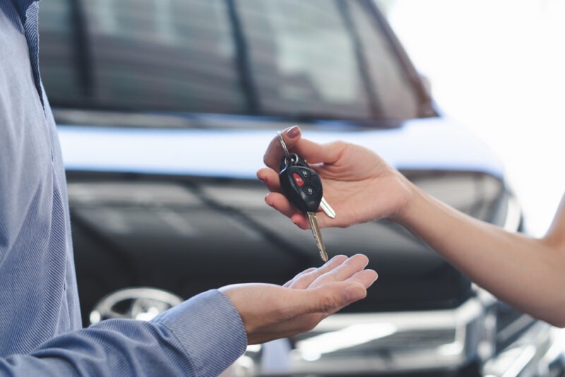 A close-up of a woman's hand giving keys to a man's hand at a dealership.