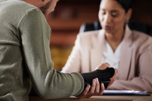 A man with a broken arm sits at a desk with a woman, both engaged in conversation.