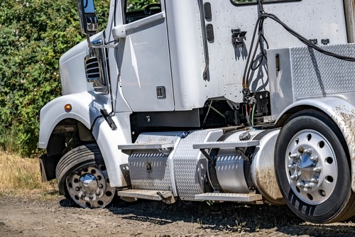 A semi truck with a flat tire parked on the side of the road, surrounded by grass and a clear blue sky.
